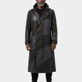 A man wearing a long black leather coat with diagonal paneling, photographed against a plain light gray studio background.